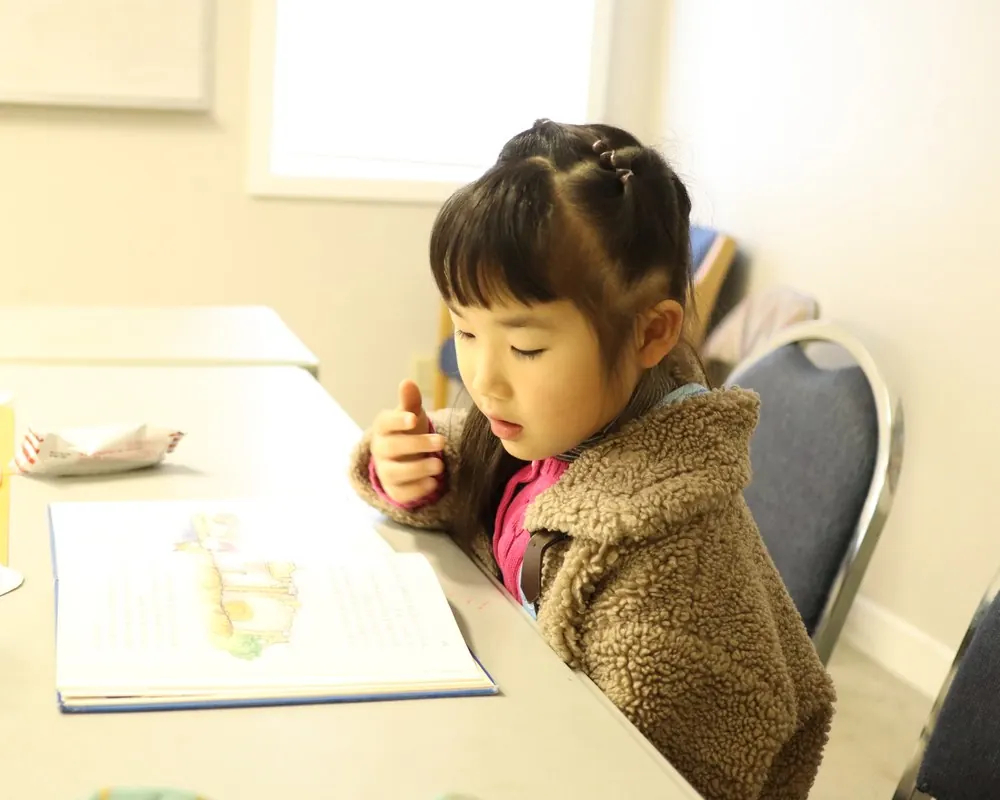 주일학교 책상에서 성경 그림책을 손가락으로 짚으며 읽는 아이