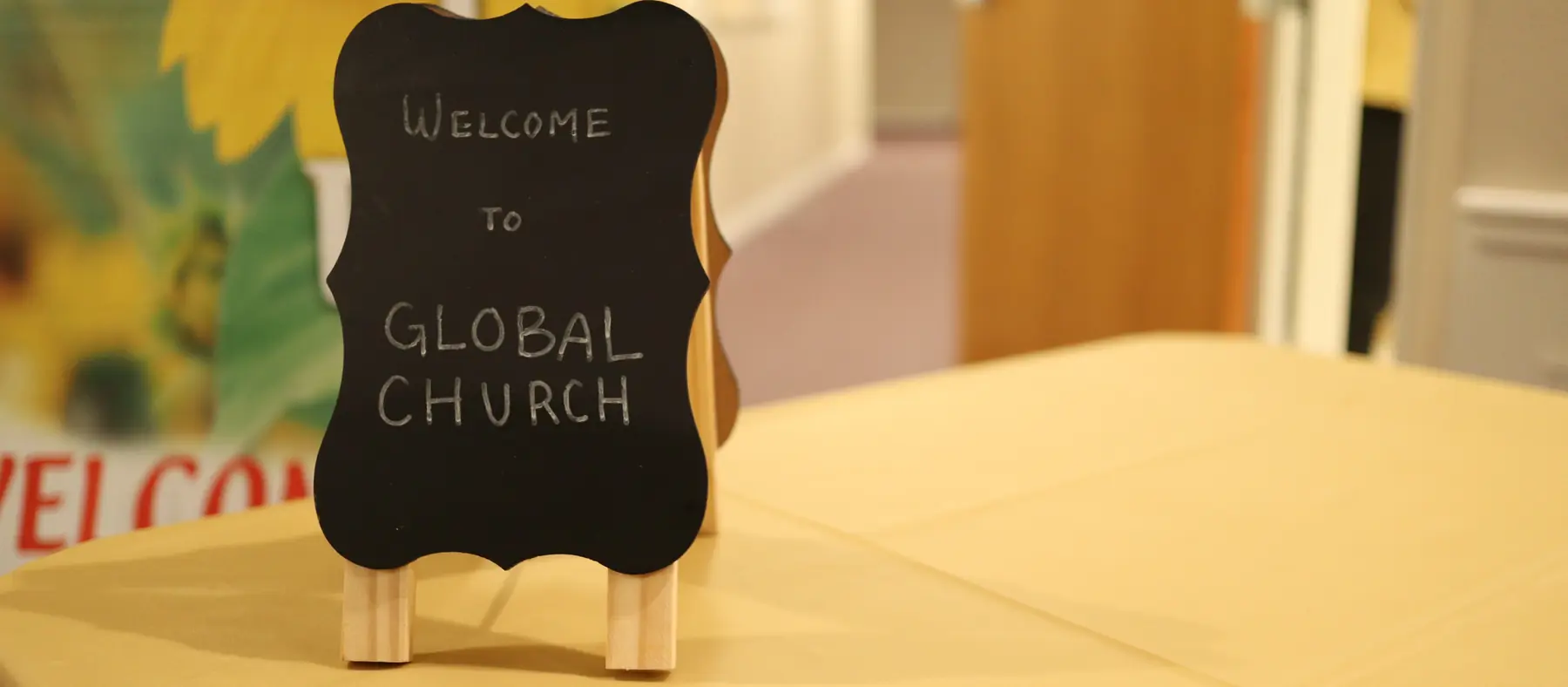 교회 친교 탁자 위 "WELCOME TO GLOBAL CHURCH" 손글씨 칠판과 환영 현수막